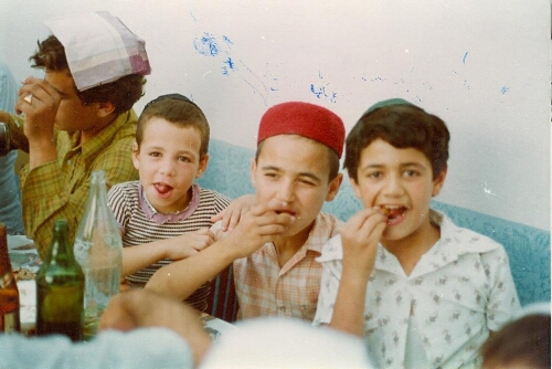 Scène de repas en extérieur avec trois portraits de face d'enfants, lors d'une cérémonie de circoncision, Djerba